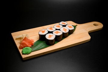 Portion of sushi rolls served on leaves and wooden board isolated