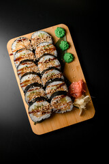 Sushi rolls on a wooden board with sauce and sesame