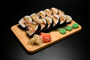 Sushi rolls on a wooden board with sauce and sesame on wooden board