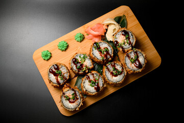 Sushi rolls with sauce on a wooden board served with ginger and wasabi