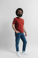 Fashionable man with a beard wearing a red tee, denim jeans, and a wide-brimmed hat, striking a...