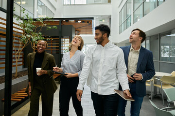 Four multiracial young adults in businesswear walking and laughing in corridor of office
