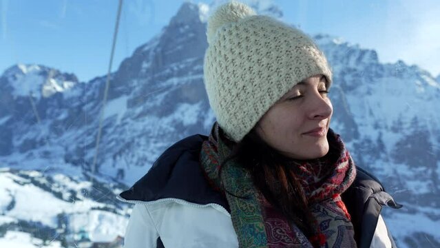 Woman wearing winter clothes enjoying Swiss alps view from high above in mountain peak staring at scenic view