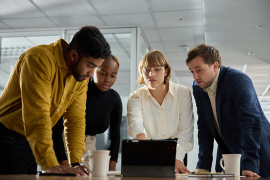 Four young multiracial adults in businesswear having meeting around digital tablet in office