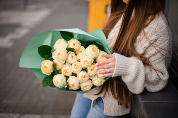 Hands of a woman hold a large bouquet of white roses in a green wrapper