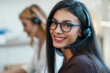 Successful attractive businesswomen working with laptops while talking with earphone on coworking...