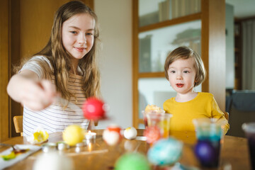 Big sister and her brother dyeing Easter eggs at home. Children painting colorful eggs for Easter hunt. Kids getting ready for Easter celebration.