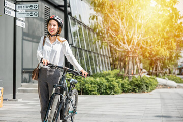 A cheerful Asian businesswoman helmeted and in suit stands with her bicycle symbolizing the modern...