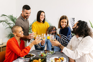 Happy group of multi-generational family gathered around dinner table toasting wine celebrating together at home