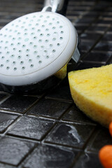 Close up of dirty shower head, cleaning sponge and a spray bottle on the shower floor