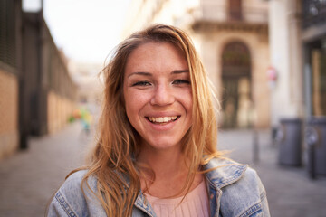 Close up portrait of cheerful attractive young Caucasian woman happy smiling face on street. Female people with joyful expression looking at camera outdoor. Blonde gen z girl posing natural for photo - obrazy, fototapety, plakaty