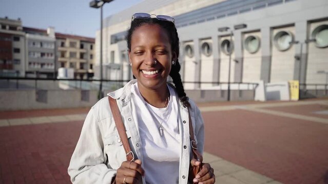 Portrait of beautiful African woman smiling at camera looking confident. Happy young latina girl of carefree with a broad smile. Positive people wearing white clothes, urban city outdoors. 