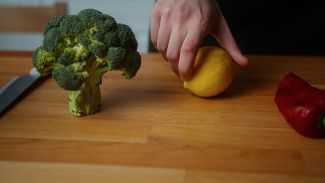 Close-up of a man hand turns a lemon on the kitchen table with red peppers and broccoli	