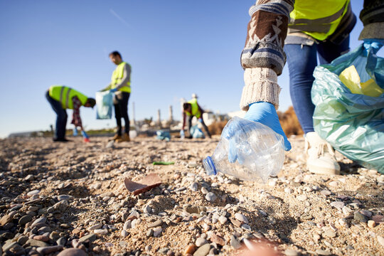 Group of cleanup volunteers cleaning up waste in nature and holding a garbage bag trash. Close up of activist hand picking up a plastic bottle. Concept of environmental protection.