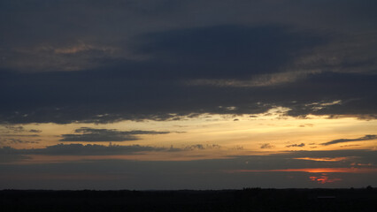 Panoramic view of a golden sunset sky with dramatic, dark grey clouds. The beautiful evening...