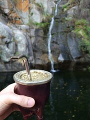 Tradiciones Naturales: Disfrutando un Mate con Vista a una Cascada que Fluye sobre Piedra hacia un Espejo de Agua