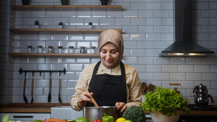Beautiful woman with headscarf cooks soup at home in modern kitchen 
