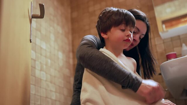Nurturing scene of mother drying son after bath, bedtime night routine of nurturing mom taking care of her child seated inside bathroom. kid covered with towel receiving maternal affection