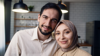 Close up young married couple hugging each other in the kitchen, smiling and looking at the camera	
