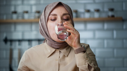 Headscarved woman taking her medicine while sitting in the kitchen	