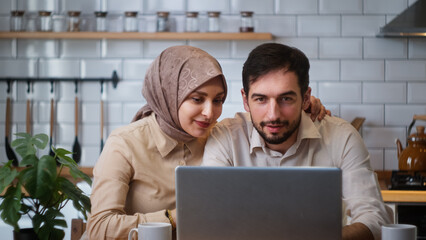 Beautiful young couple talking distance video call looking at laptop webcam in kitchen. Remote calling, live video call with family or friends concept