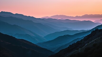  a view of a mountain range at sunset from the top of a mountain in the distance is a pink and blue sky with a line of mountains in the foreground.