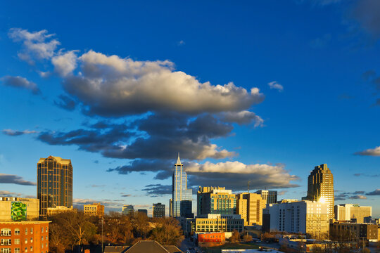 A downtown city skyline of Raleigh, North Carolina under a cloudy sky at sunset.