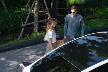 Young couple travel with EV electric car charging in green sustainable city outdoor garden in...