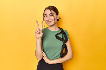 Fitness young woman with resistance bands showing number two with fingers.