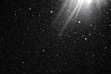 Floating dust particles. White dust  texture on a black background with a bright ray of light coming through. Snowflakes falling at night from the sky. 