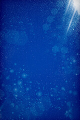 Floating dust particles on a vibrant blue background. White dust texture and a beam of bright rays of light coming through. Textured Blue background with bokeh light rays