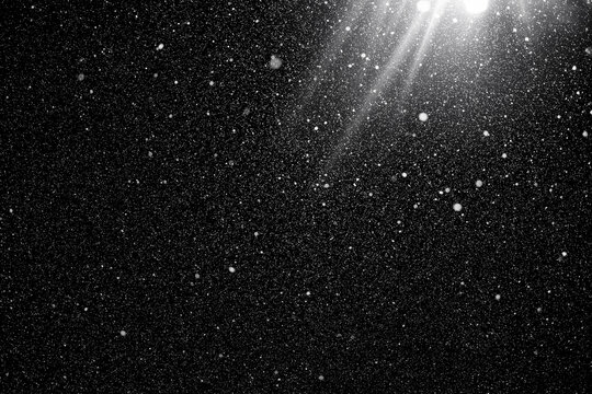 Floating dust particles. White dust texture on a black background with a bright ray of light coming through. Snowflakes falling at night from the sky.