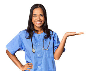Young Filipina nurse posed in studio showing a copy space on a palm and holding another hand on waist.