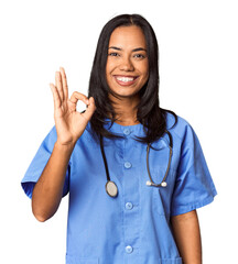 Young Filipina nurse posed in studio cheerful and confident showing ok gesture.