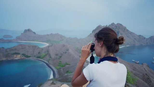 Female photographer. Brunette woman takes pictures on the beach with analog camera in Komodo island