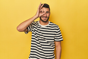 Young Hispanic man on yellow background excited keeping ok gesture on eye.