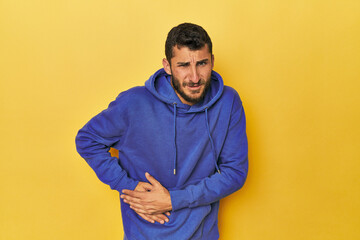 Young Hispanic man on yellow background having a liver pain, stomach ache.