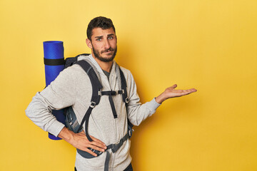 Young Hispanic man ready for hiking showing a copy space on a palm and holding another hand on...