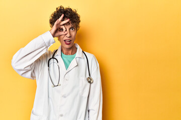 Caucasian mid-age female doctor on yellow studio excited keeping ok gesture on eye.