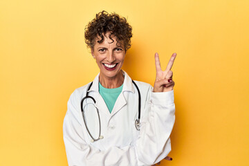 Caucasian mid-age female doctor on yellow studio showing number two with fingers.