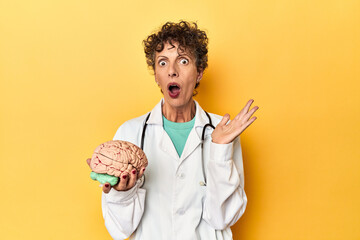 Doctor holding a brain model on yellow studio surprised and shocked.