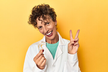 Doctor with invisible dental aligner on yellow joyful and carefree showing a peace symbol with...