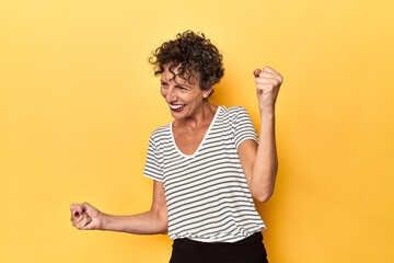 Mid-aged caucasian woman on vibrant yellow dancing and having fun.