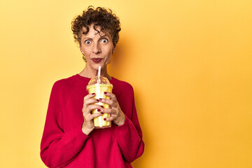 Woman sips a vanilla shake on a vivid yellow studio background