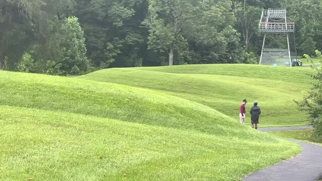 Multiracial father and son explore Great Serpent Mound Earthworks in Peebles, Ohio. Slow motion footage shows walking path, and long serpentine curving mound making the body of the snake. 