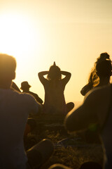 Silhouette of woman instructing yoga class outdoors at sunset 