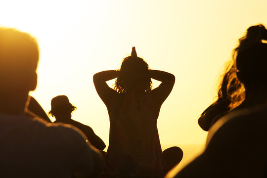 Silhouette of woman instructing yoga class outdoors at sunset 