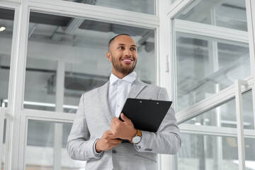 Fototapeta premium Happy man with clipboard in office, low angle view. Lawyer, businessman, accountant or manager