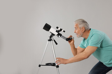 Senior astronomer with telescope on grey background. Space for text