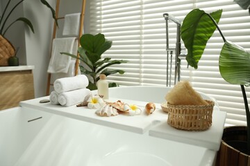 Bath tray with spa products, towels and shells on tub in bathroom
